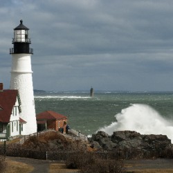Waves Crash By Portland Head Lighthouse as Sun Breaks Through Clouds