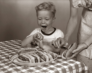 1950s EXCITED BOY AT TABLE WITH HOT DOGS ON BUNS 187043