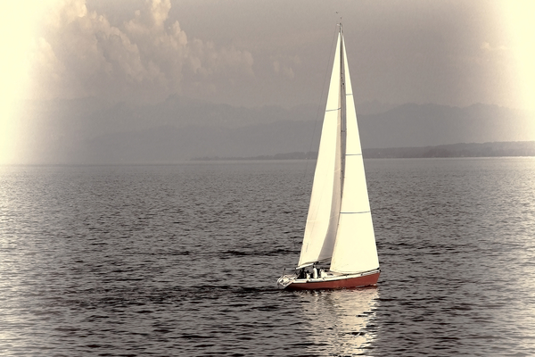 Sailboat with red hull glides across calm waters on a sunny serene day. by IB Photography