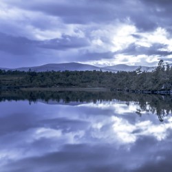 The tranquil lake reflects the cloudy sky creating a mirror image of natures beauty on a moody day.