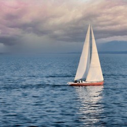 A sailboat cuts through the water under a vibrant sky during a beautiful sunset.