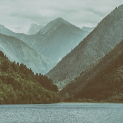 Picturesque vista of mountains lush forests and tranquil lake on a cloudy atmospheric day.