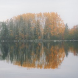 A serene autumn island scene with colorful trees reflected in tranquil waters.