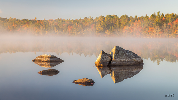 Rocks in a calm lake on a cool fall morning by Hugh Chisholm Photography