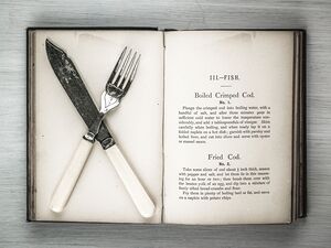 Old cookery book open with an old fork spoon and table knife