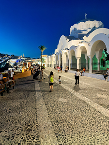 Santorinis iconic white church and bustling street at dusk.