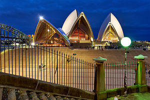 Sydney Opera House illuminated at dusk with crowds on steps.