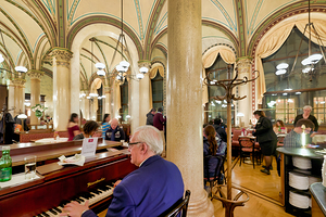 Man playing piano in an ornate bustling cafe.