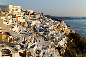 Santorinis white buildings cascade down cliff to the sea.