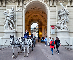 Historic archway with statues horse carriage and pedestrians.