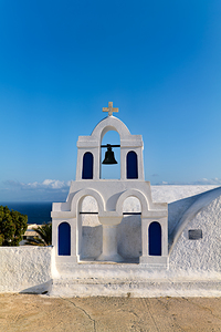 White bell tower against blue sky and sea.