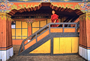 Young monk in red robes on colorful temple staircase.