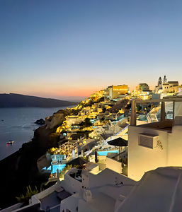 Illuminated cliffside village at sunset over the ocean.