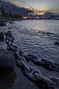 Old rusty chain lying on a rocky beach at sunset