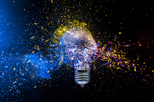 Light bulb exploding in colorful powder on black background