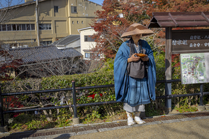 Buddhist monk holding a bowl standing near a sign in japan