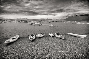 Colorful kayaks resting on a rocky beach awaiting kayakers in ic