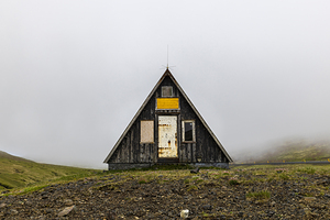 Small abandoned a-frame wooden hut standing on  foggy day