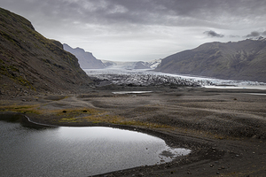 Small lake reflecting cloudy sky in front of glacier tongue in i