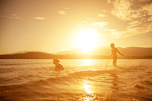 pair of children playing in the sea shot taken at sunset