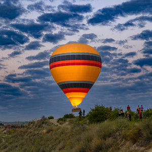 hot air balloon flies over the tourists near the hills of goreme