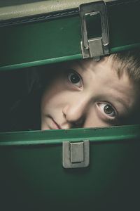 child hides in an old green suitcase