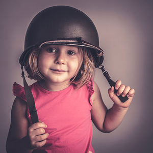 Caucasian little girl wearing a military helmet.