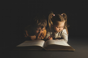 children lying reading a book