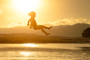 3 year old girl jumps into the sea at sunset.