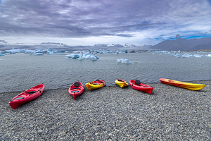 Colorful kayaks resting on a rocky beach awaiting kayakers in ic