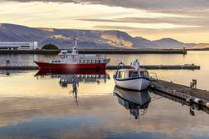 Two boats reflecting on calm water at sunset in reykjavik harbor