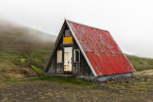 Old abandoned wooden hut with red roof standing on green hillsid