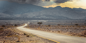 Empty asphalt road winding through a dramatic desert landscape