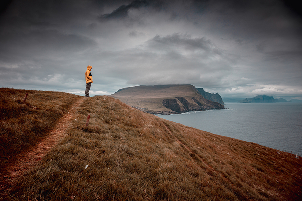 man with yellow rain jacket standing on top of a mykinese cliff 