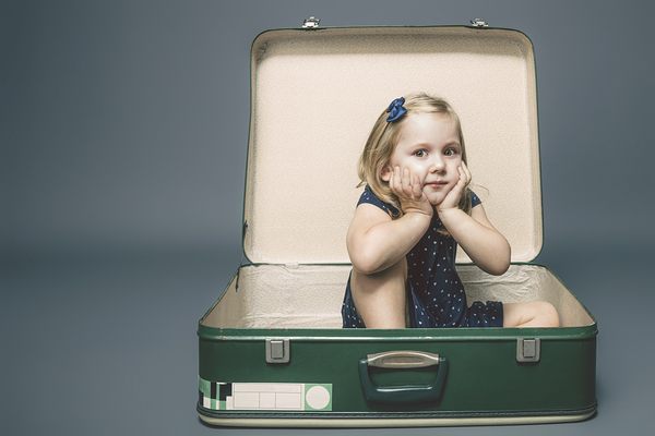 girl with dreamy expression sitting inside a vintage suitcase.