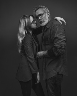Black and white portrait of a trendy couple wearing glasses standing in front of a grey background