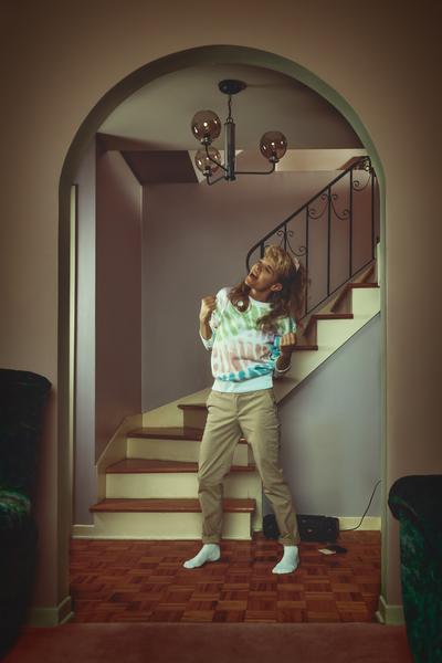 vintage lifestyle portrait of a young blonde woman in a late 80s early 90s interior decor singing to music playing on a tape recorder in front of a staircase by Artmood Visualz