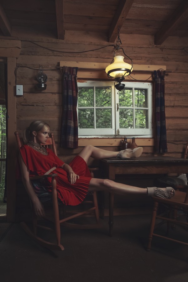 Beautiful young blonde woman sitting on a chair made of wood with her leg on the table inside a rustic wooden shack by Artmood Visualz