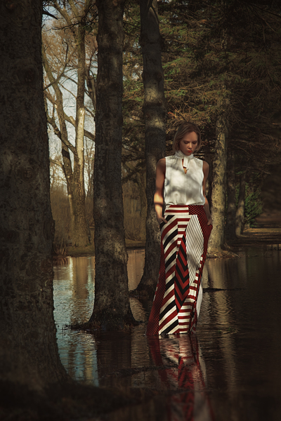 Beautiful young blonde woman wearing a long red patterned skirt standing in a water flooded forest by Artmood Visualz