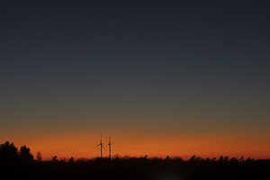 A couple of wind turbines at sunset over a field of trees. The concept of combining nature and renewable energy