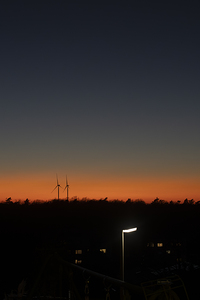 A couple of wind turbines at sunset over a field of trees. The concept of combining nature and renewable energy