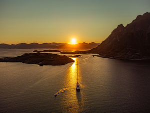 Sailboat in Lofoten Norway under the midnight sun. Mountains in the horizon clear skies near Henningsvaer orange sunset.	