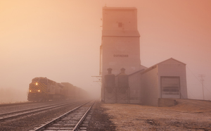 intermodal train passes a farmers grain storage elevator