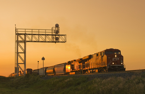 locomotives pulling rail hopper cars pass an overhead rail signal 