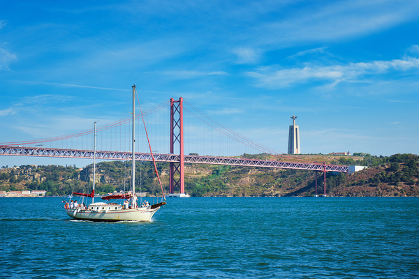 View of 25 de Abril Bridge over Tagus river Christ the King monument and a yacht boat. Lisbon Portugal by Dmitry Rukhlenko