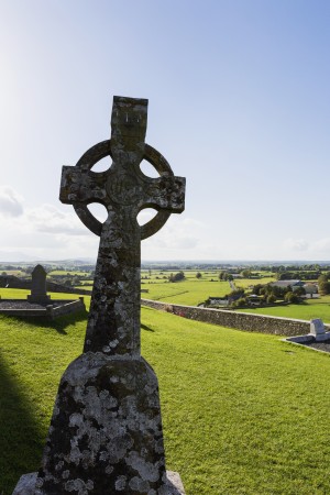 Celtic cross on grassy hill with stone wall under blue sky; Cashel, County Tipperary, Ireland
