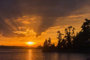 Sunrise casting an orange glow over the sky and reflected in a tranquil lake; Ontario, Canada