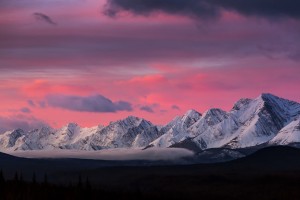 Dramatically glowing sky at sunrise with snow covered mountain range and fog in the valley; Kananaskis Country, Alberta, Canada