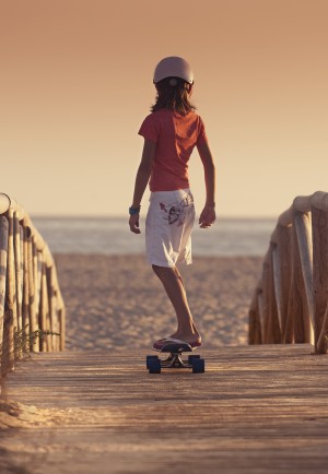 A Young Person Skateboarding With Bare Feet Over A Wooden Boardwalk Towards The Beach; Tarifa, Cadiz, Andalusia, Spain