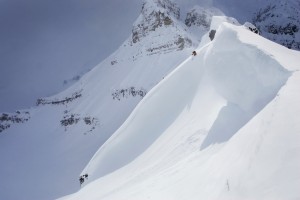 Skier On Crest Of Big Drop, Dwarfed By Mountain; Canada, British Columbia, Icefall Lodge